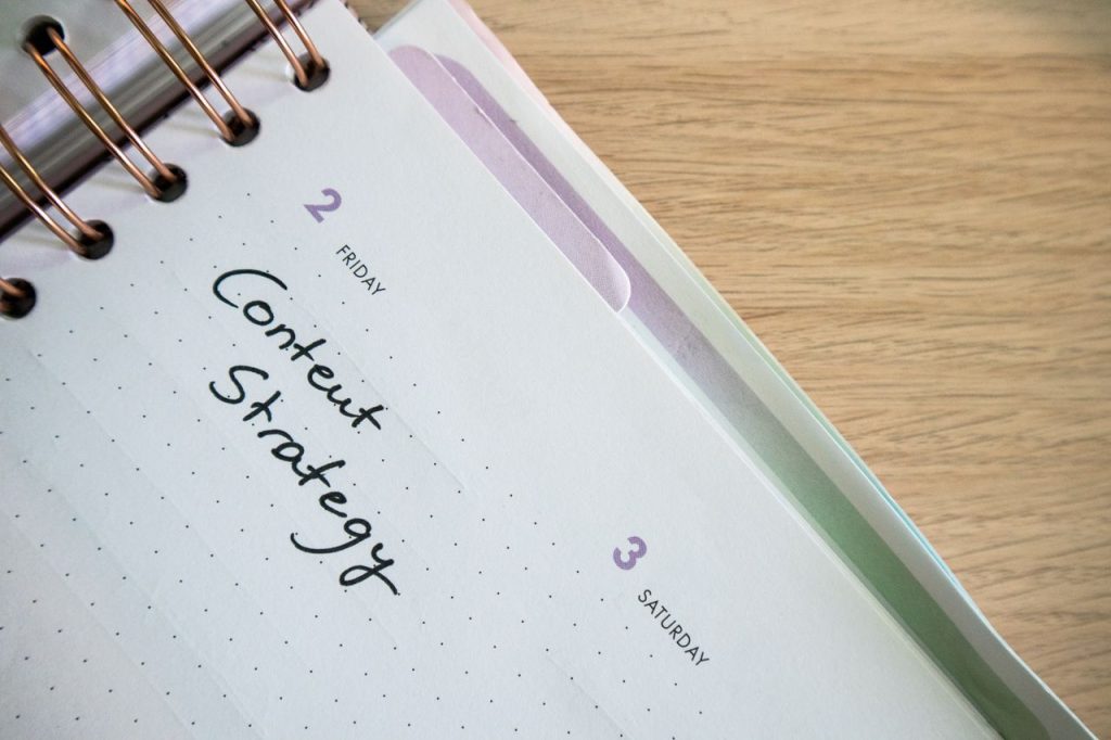 Top view of a notebook open to a day planner featuring 'Content Strategy' handwritten, lying on a wooden desk.