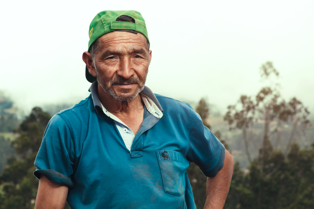 A rural farmer in a blue shirt and green cap poses outdoors in Cajamarca, Peru.
