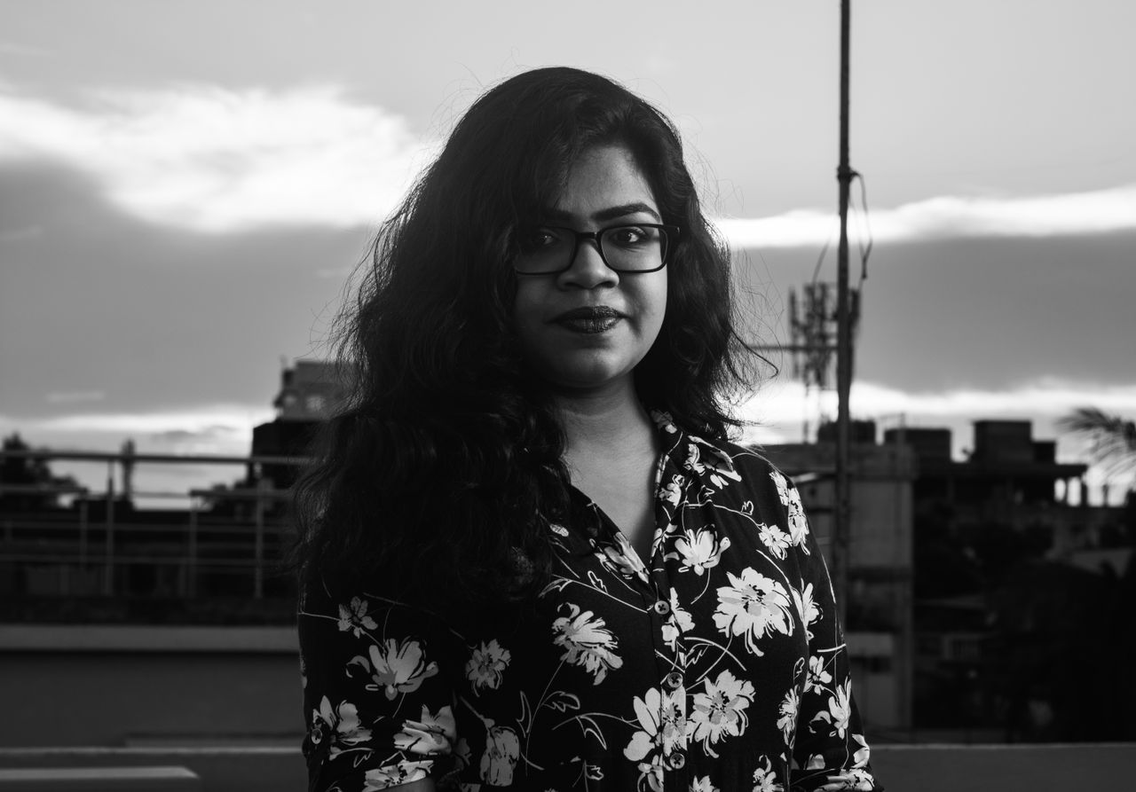 Black and white portrait of a woman in glasses with a floral shirt during twilight.